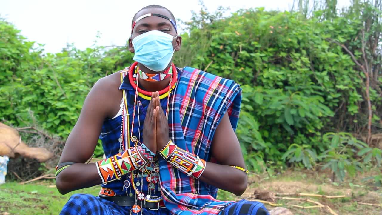 un hombre africano con una máscara protectora en un atuendo tradicional maasai saluda