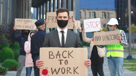 businessman wearing facial mask and suit holding back to work" signboard and looking at camera in a protest against covid 19"