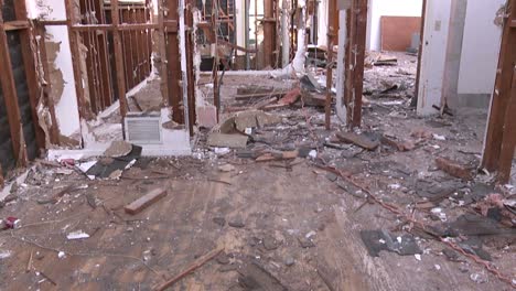 tilt up from a debris covered floor to show the exposed beams and crumbling walls of a house in the process of being demolished