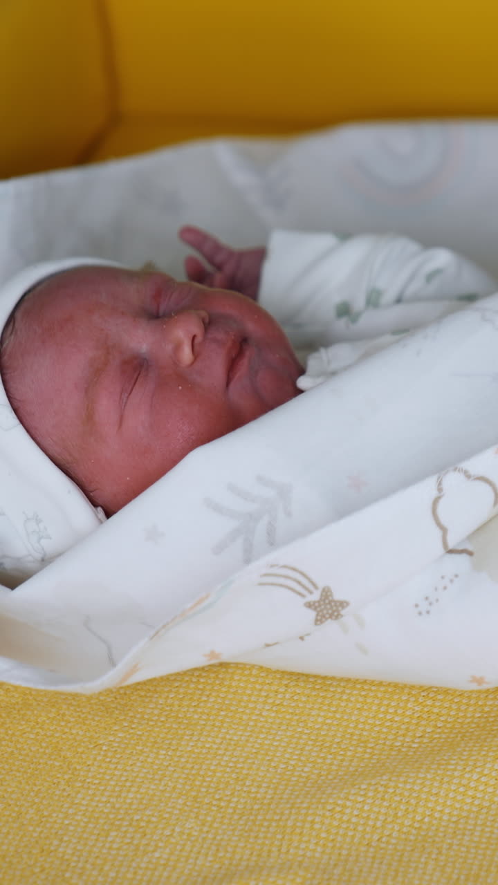 Tiny newborn wearing white cap and bodysuit. Medic in gloved hands covering the child in a wrap. Close up. Vertical video