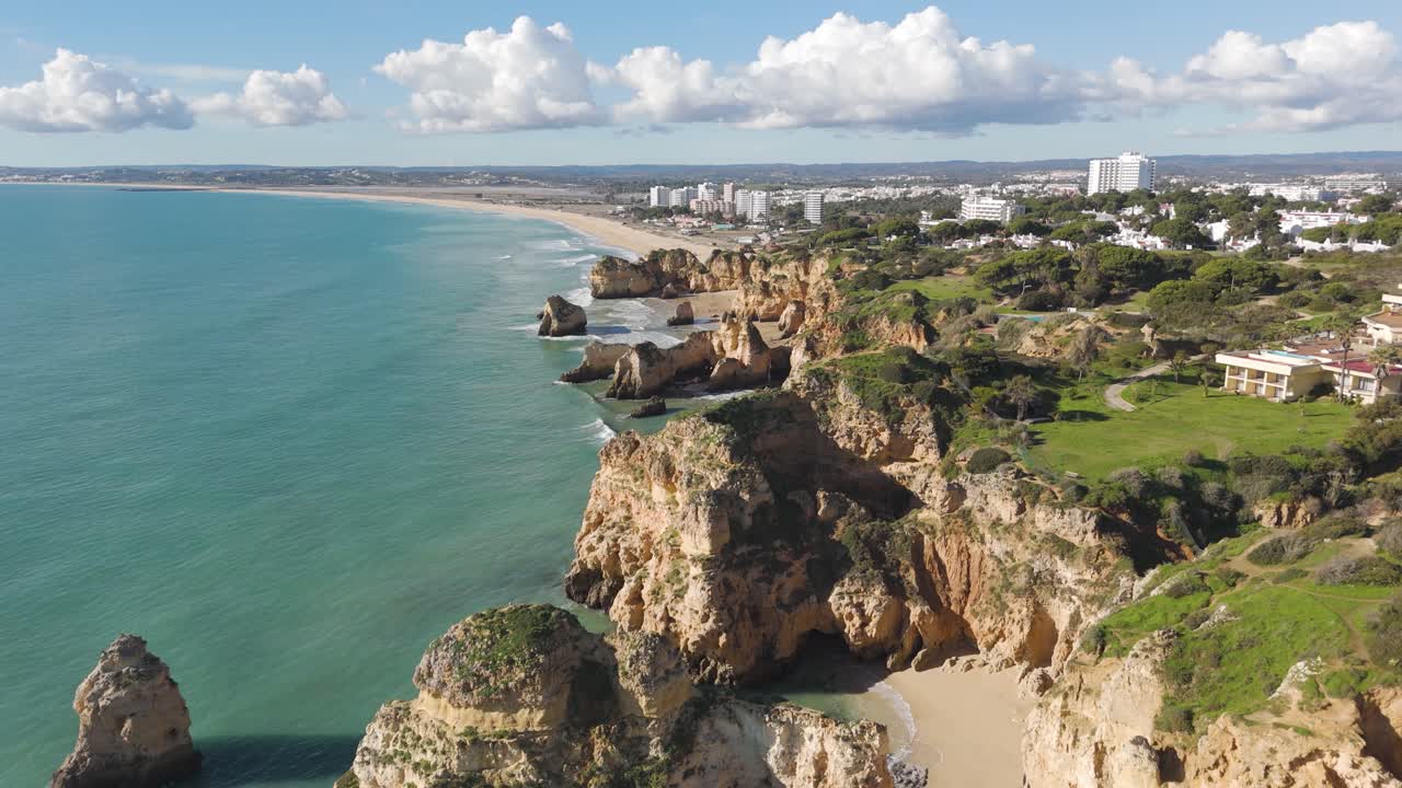 Luftfoto i fremoverbevegelse langs Algarves ulendte kystlinje, som viser klipper og den fjerne landsbyen Alvor.
