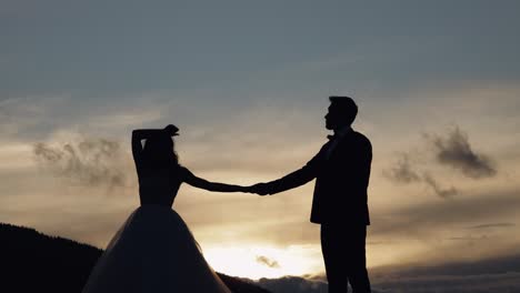 Siluetas-De-Recién-Casados-Novia,-Novio-Bailando-En-La-Ladera-De-La-Montaña,-Tomados-De-La-Mano,-Familia-De-Pareja-De-Novios