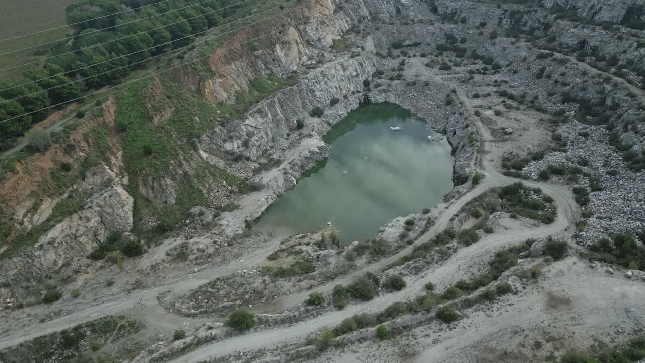 Green water has accumulated at the bottom of an abandoned quarry near sant fost de campsentelles, barcelona, surrounded by rocky terrain and vegetation