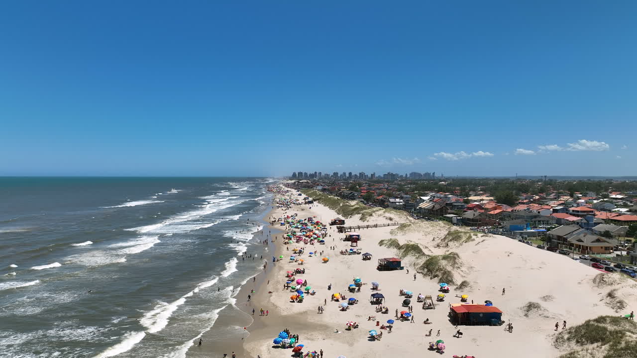 Video 4K 60fps quay từ trên không bằng drone toàn cảnh vùng biển mùa hè cổ điển với cồn cát, biển xanh trong vắt, khách du lịch và đường bờ biển ở Imbé Rio Grande do Sul Brazil.