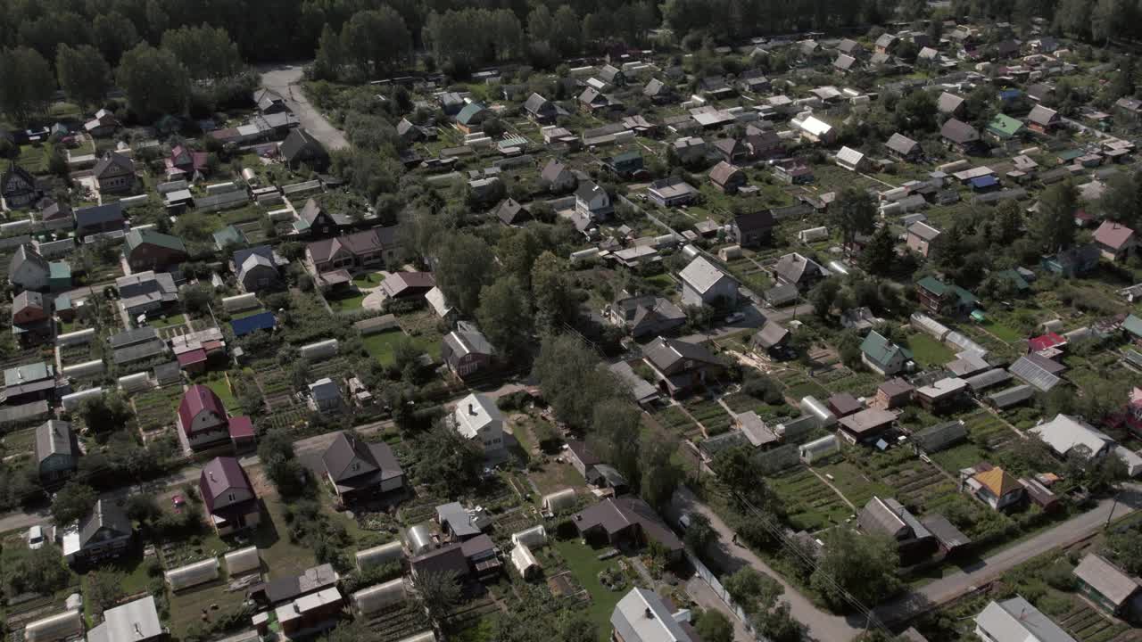 Drone footage of a quiet rural settlement with detached houses, vegetable gardens, and tree-lined streets, surrounded by forested landscape in the Ural, Russia