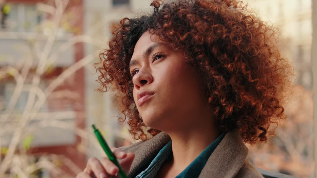 Thoughtful Young Woman with Curly Hair Looking Out on Balcony