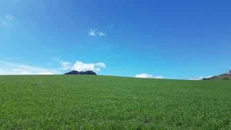 volando con un dron sobre un prado verde con unas montañas espectaculares en el fondo con un cielo azul con nubes blancas