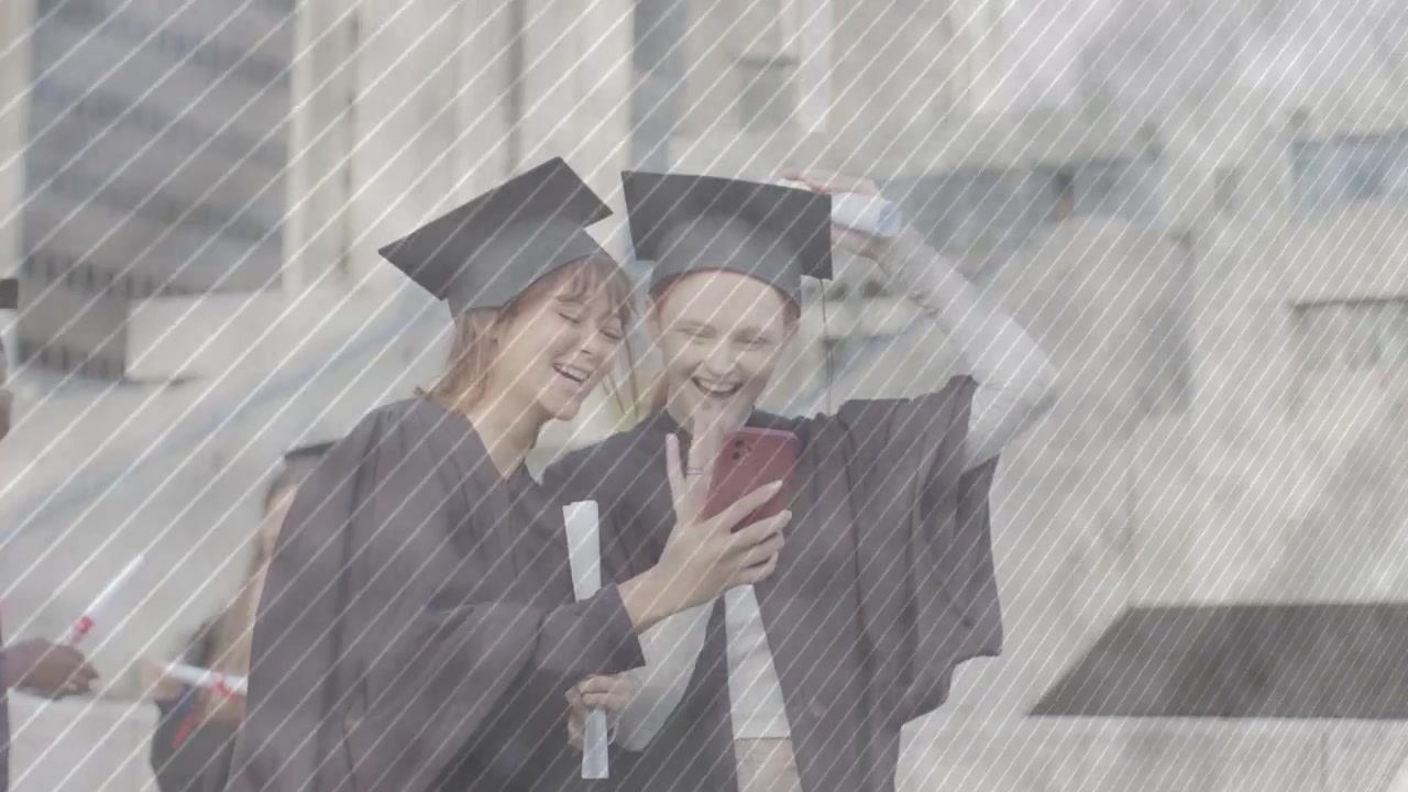 Due laureati che si chinano verso un telefono che mostra un messaggio nella piazza del campus, sistemandosi i cappelli, per la laurea