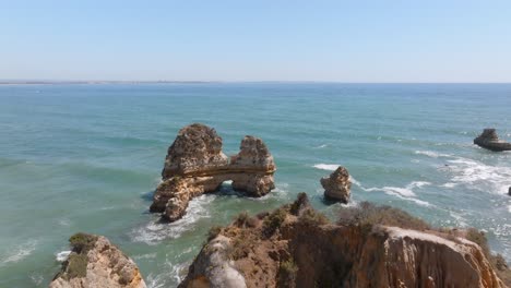 ridgeline leads out to oceanic arch battered by ocean waves crashing, lagos algarve portugal