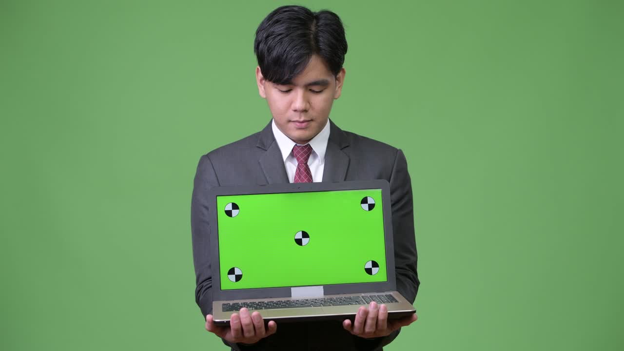 젊은 잘생긴 아시아 사업가 노트북을 보여줍니다.