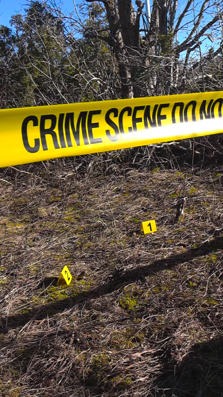 Bright yellow crime scene tape restricting access to an outdoor area with evidence markers placed on the ground, signaling a police investigation in progress on a sunny day