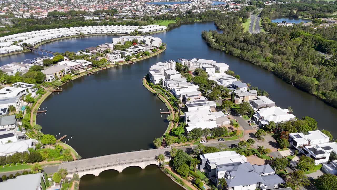 Sunny daytime drone flyover of modern lakeside residential neighborhood with bridge and greenery