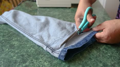 hands of female tailor cut jeans leg shorter with scissors, sewing skills