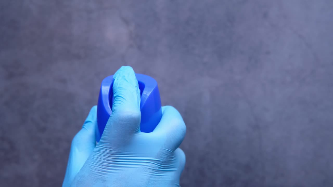 mano con guantes sosteniendo una botella de spray azul