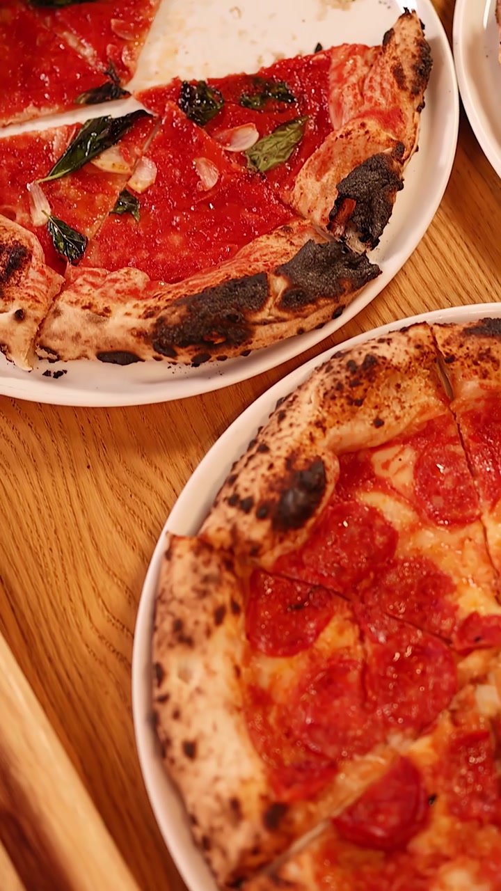 Vista dall'alto di persone che condividono varie pizze napoletane con salsa di pomodoro e basilico fresco.