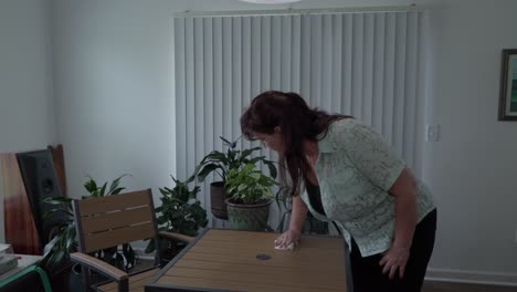 Middle aged caucasian woman spraying kitchen table and wiping it