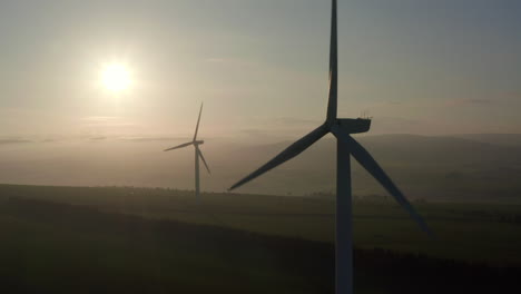 Eine-Luftaufnahme-Von-Zwei-Windparkturbinen,-Die-Sich-Langsam-Drehen,-Mit-Der-Abendsonne-Im-Hintergrund,-Aberdeensire,-Schottland