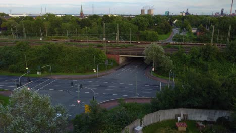 large-white-truck-is-driving-down-a-long-winding-road-surrounded-by-lush-green-trees-and-grass-bridge-in-the-distance-people-travel-to-work-motorbike-several-buildings-visible-in-the-background