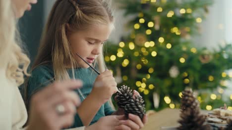 cheerful caucasian mother and daughter decorating cone with white paint.