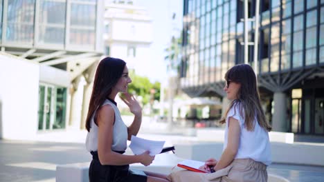 hermosas mujeres de negocios hablan de un contrato concluido a la hora del almuerzo cerca del edificio de oficinas. concepto de negocios. mujeres de moda se sientan y tienen una reunión informal