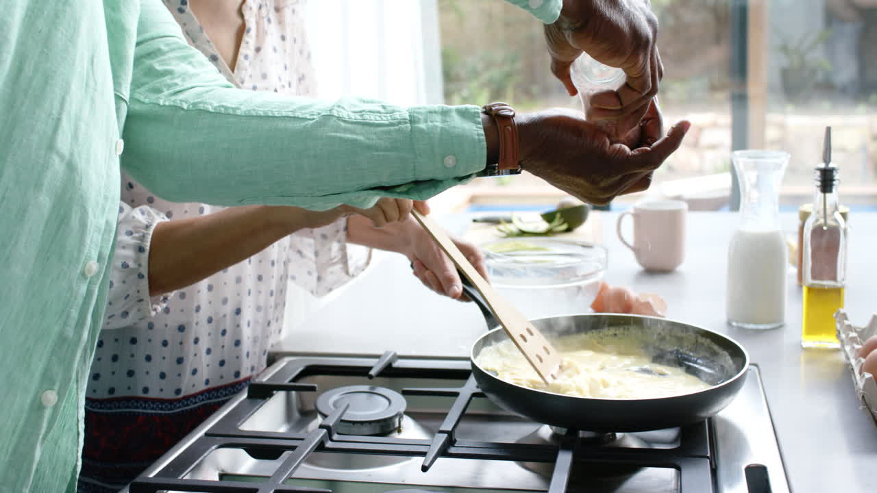 pareja biracial cocinando y sazonando tortilla en la sartén en la cocina, cámara lenta