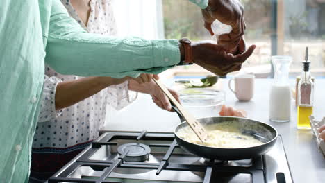 Pareja-Birracial-Cocinando-Y-Sazonando-Tortilla-En-Sartén-En-La-Cocina,-Cámara-Lenta