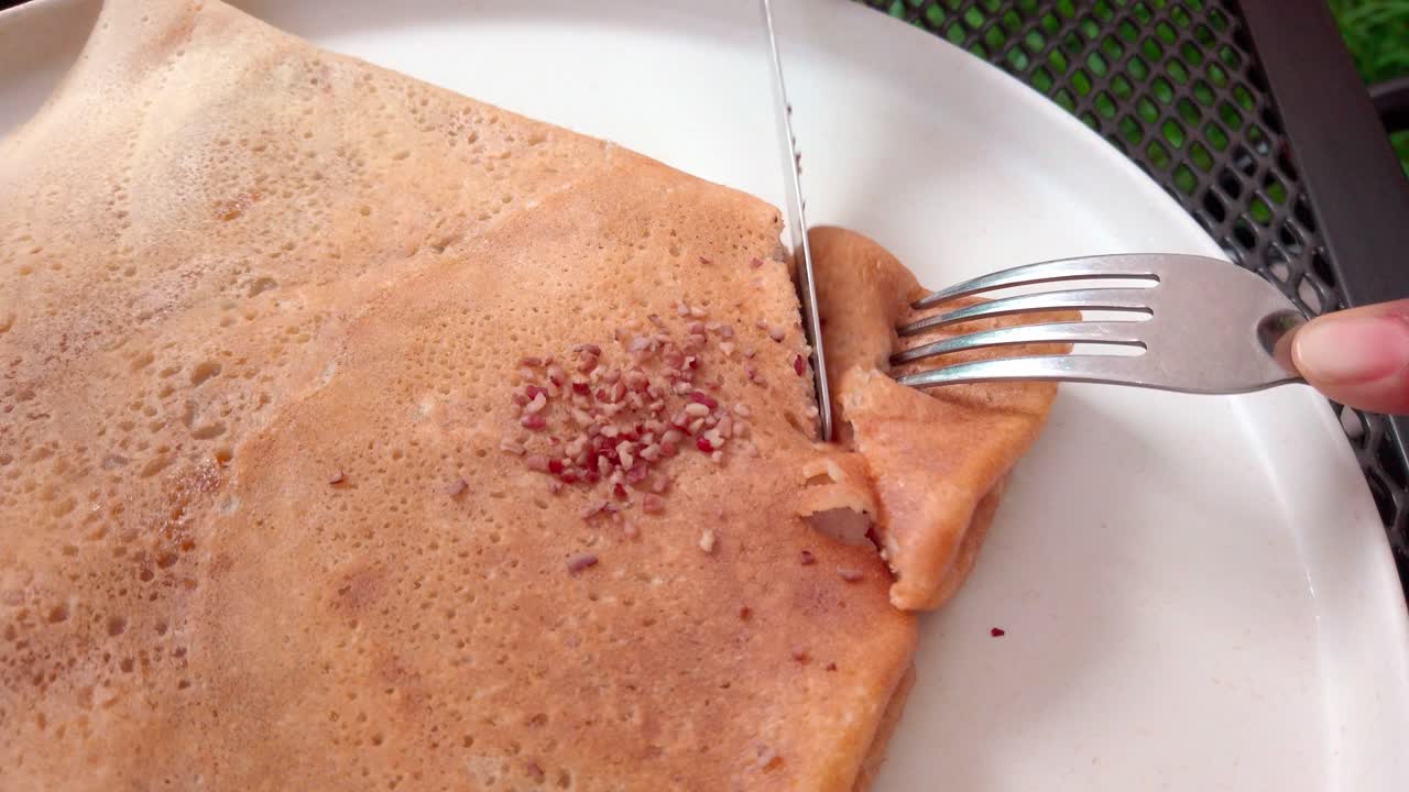 Crispy dosa being cut open with fork and knife on white plate outdoors
