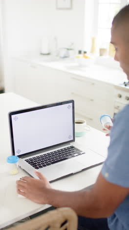vertical video of anglo indian man holding medication making video call using laptop, copy space