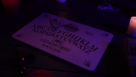 close up video of a wooden ouija board on a table surrounded by candles and a cross in a muffed - close up video of a wooden ouija board on a table. wax candles and a cross around. the planchette is slowly moving across the board, spelling out words and numbers. creative mystical content