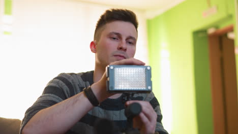 person adjusting led video light while setting up camera equipment. focus on hands and light panel. indoor setup with a green background, relaxed atmosphere, and soft lighting
