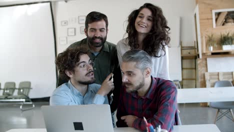 smiling coworkers talking and looking at laptop in cozy office