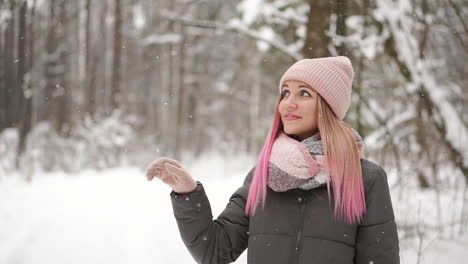 slow motion, winter woman in the woods watching the snow fall and smiling looking at the sky and directly into the camera.