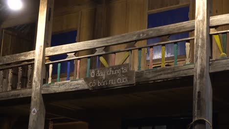 a traditional wooden balcony featuring colorful railings, illuminated warmly at night, evoking rustic charm and handmade craftsmanship. a small sign written in vietnamese says "here we sell smiles"