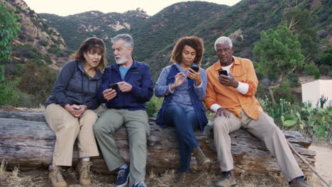 group of senior friends on hike in countryside checking mobiles phones for fear of missing out