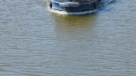 a solar-powered tour boat with tourists moves steadily along a sunlit river in prague, captured from an elevated, front-facing perspective with smooth camera tracking