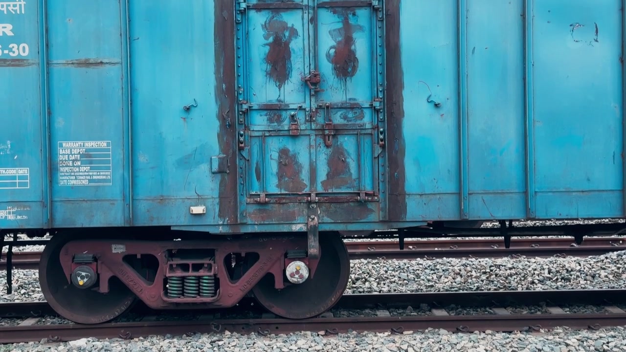 Inquadratura dal basso verso l'alto che mostra il meccanismo di bloccaggio rinforzato della porta scorrevole del carico e il carrello CASNUB su un vagone merci blu coperto delle Ferrovie Indiane.
