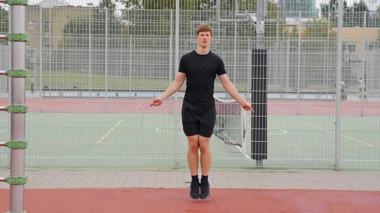 Man jumps rope by metal fence, repetitive full-body cardio movement on pavement in workout