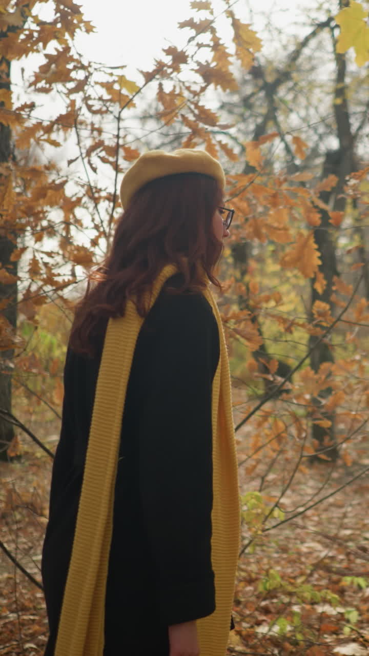 Elegant dame spaserer gjennom skogen, nyter naturens ro mens høstbladene svaier forsiktig i vinden, iført en stilig gul beret og et skjerf.