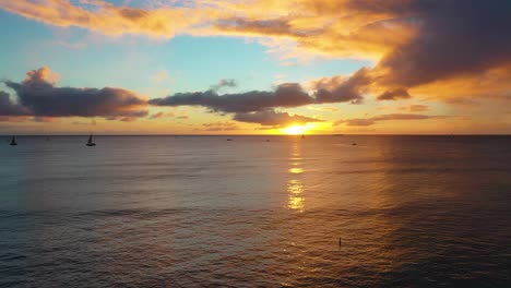 drone reveal of beautiful hawaiin ocean sunrise with boats sailing over waikiki beach in honolulu, hawaii