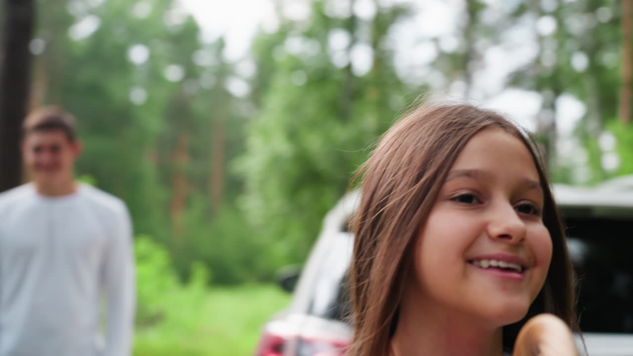 푸르른 나무들에 둘러싸여 사촌 형제로부터 피크닉 바구니를 받은 행복한 여학생이 소풍 장소로 걸어가면서 설렘에 가득 찬 미소를 짓고 있어요. 즐거운 여름 가족 나들이 순간이에요.
