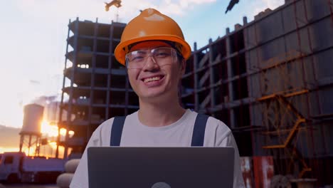 trabajador asiático usando una computadora portátil y sonriendo en el sitio de construcción