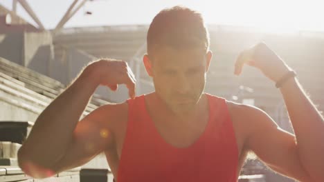 atleta caucásico estirándose en el estadio