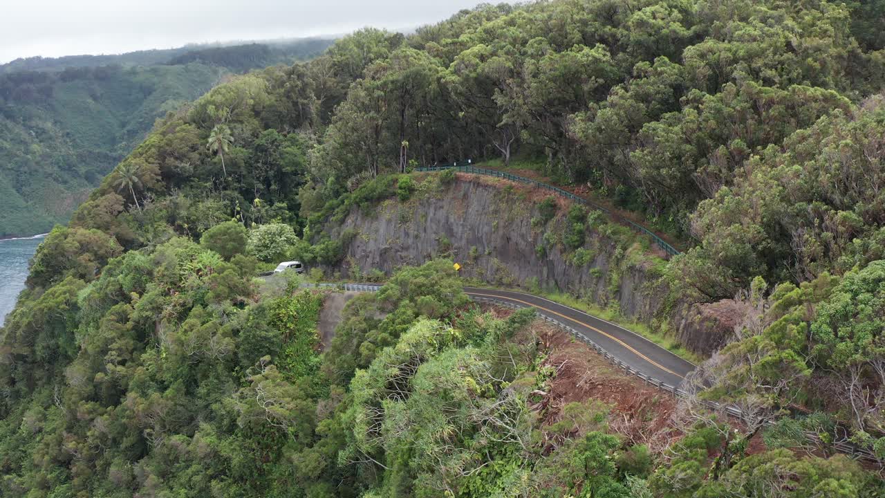 Descending close-up aerial of the windy coastal highway Road to Hana that runs through the rainforest on the windward side of Maui in Hawai'i
