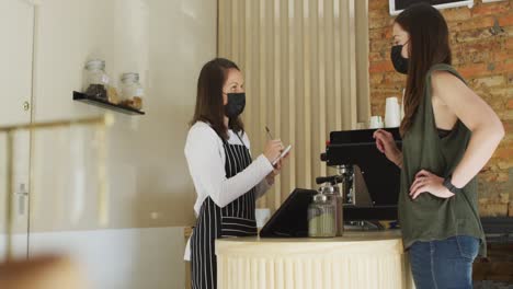 caucasian waitress wearing face mask taking order from caucasian female customer