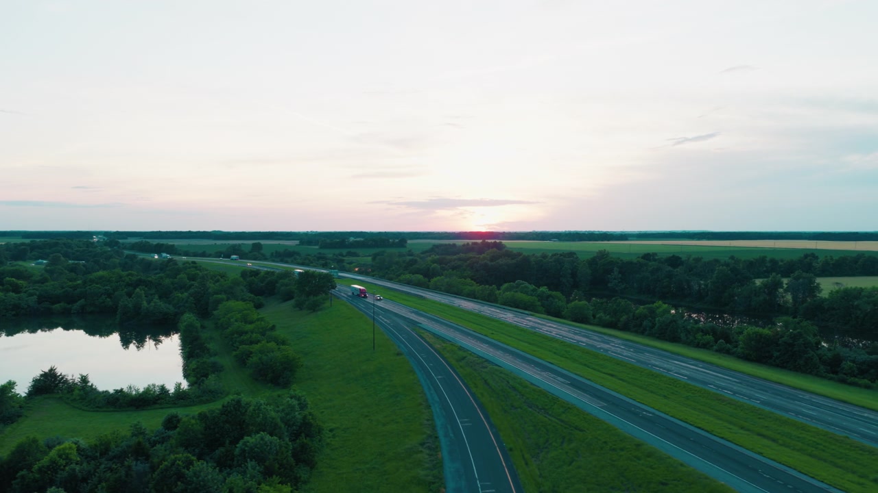 Truk semi bergerak di sepanjang Interstate 64 dan melintasi jembatan layang pedesaan saat senja — ideal untuk kampanye logistik, pengiriman kargo, rantai pasokan, dan transportasi truk. Richview, Illinois.