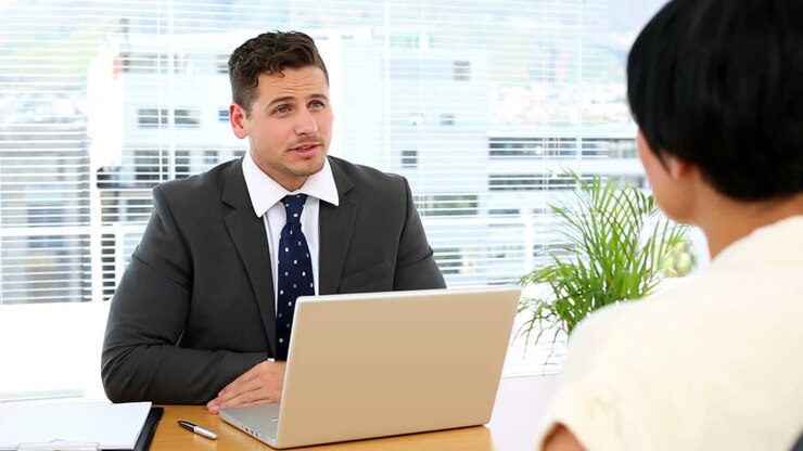 Businessman with laptop interviewing a woman at his desk
