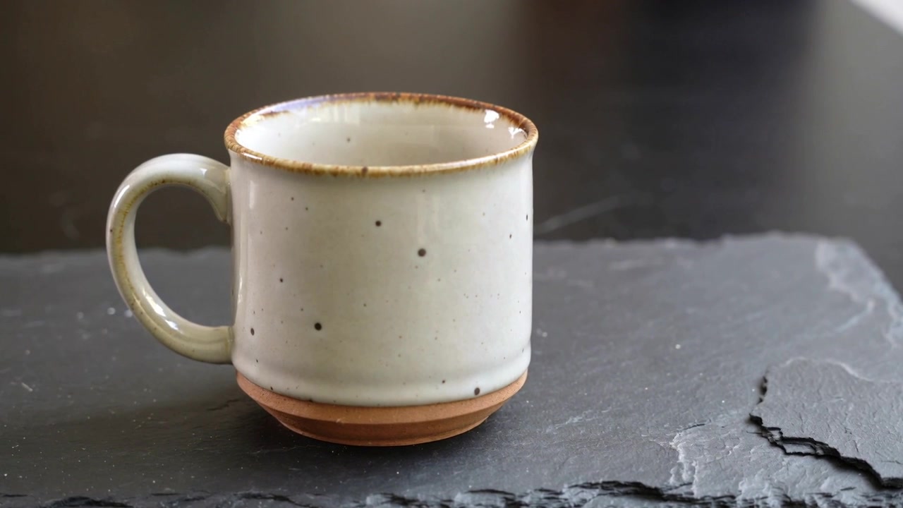 Camera pulling in, revealing speckled mug on dark table with slate crack, showing glaze texture