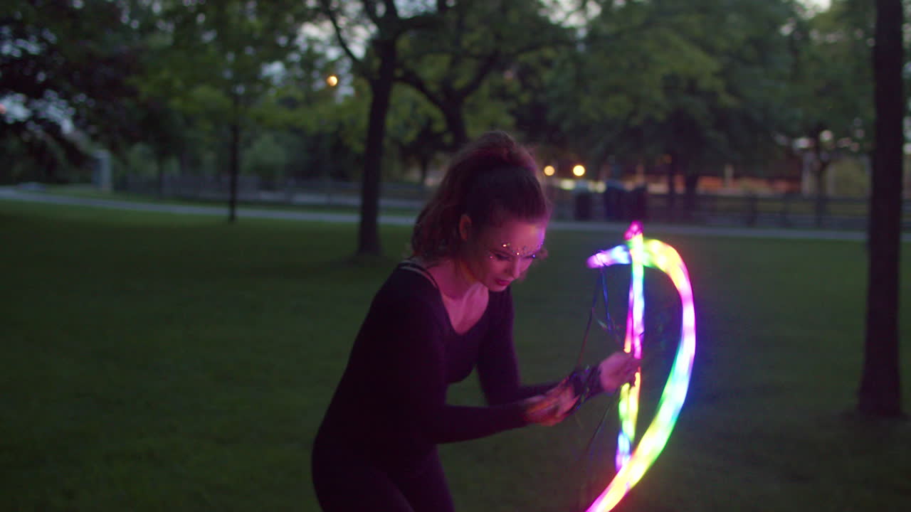 Donna che balla con ventaglio LED in un parco illuminato dal crepuscolo, primo piano medio in slow motion, panoramica a destra