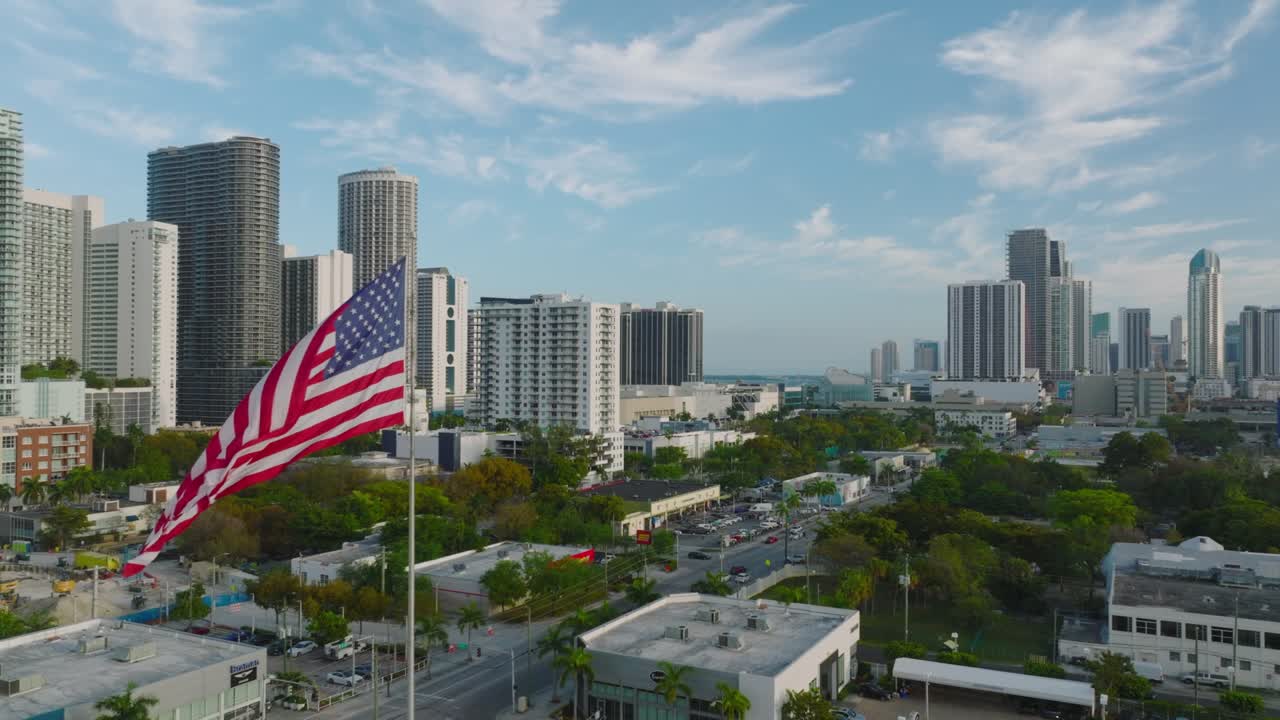 Vista aerea di un quartiere urbano con edifici e verde. Rivelazione all'indietro della bandiera degli Stati Uniti e di grattacieli residenziali sullo sfondo. Miami, USA.