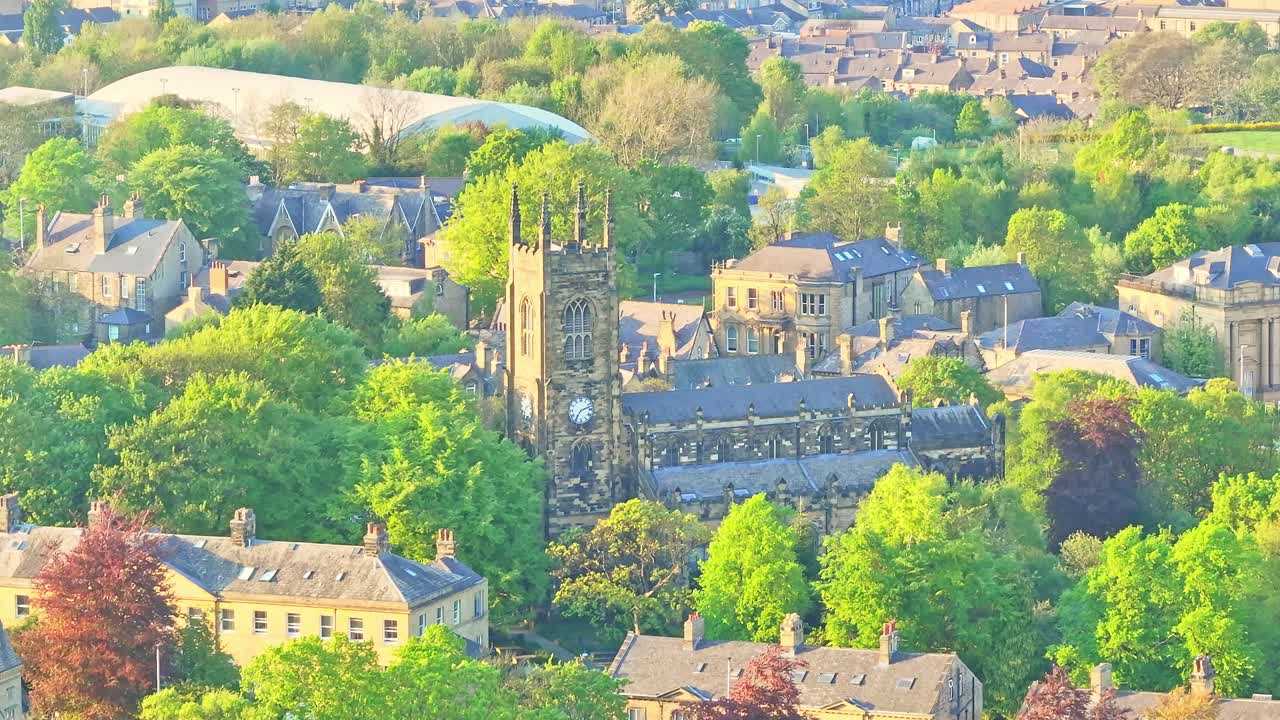 Huddersfield city centre revealing St Peter's Parish Church with its clock tower surrounded by Georgian buildings, tree-lined streets, and nearby Springwood area under soft light, drone static shot